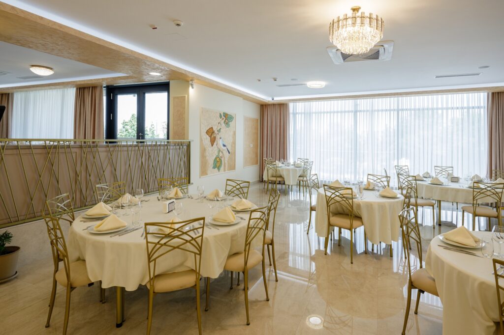 Salon restaurant aranjat festiv, cu tablouri decorative și ferestre luminoase.
